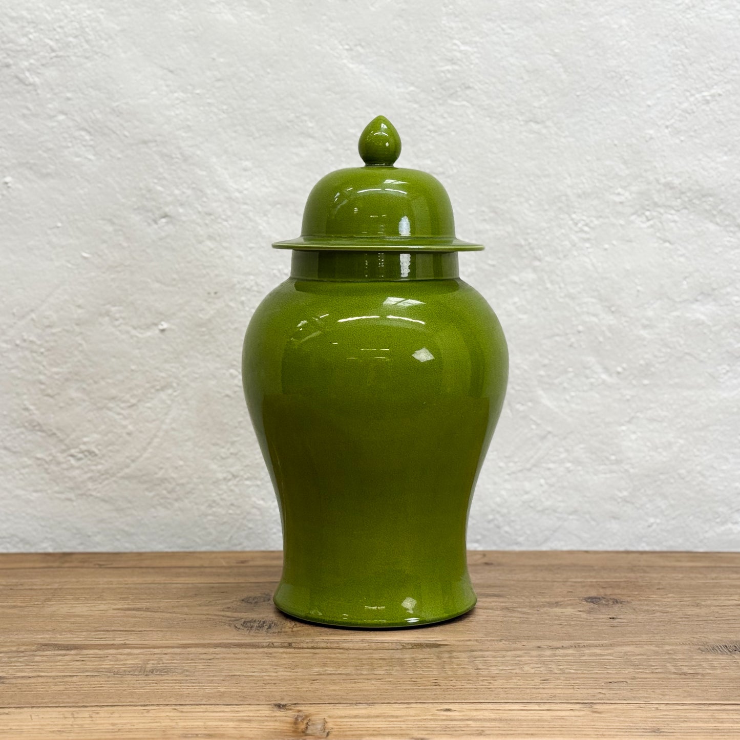 Green ceramic jar with a lid on a wooden surface and white textured background