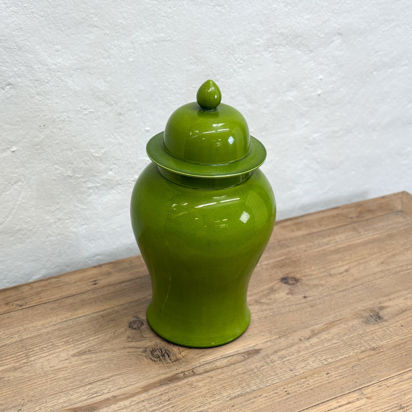 Green ceramic jar with a lid on a wooden surface against a white wall