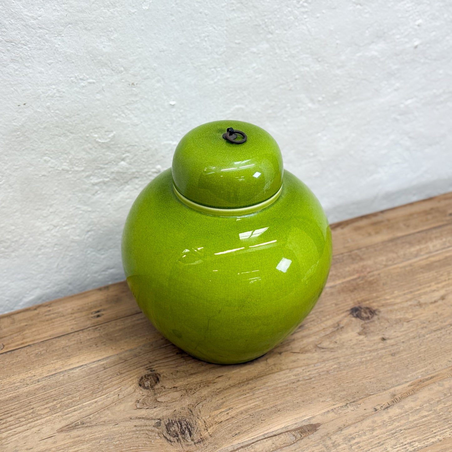 Green ceramic jar with a lid on a wooden surface against a white wall
