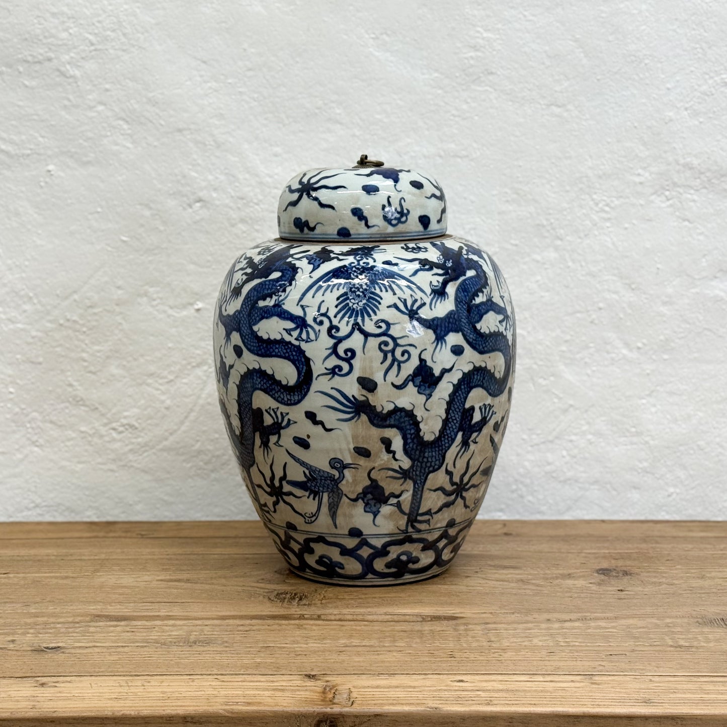 Ceramic jar with blue dragon design on a wooden surface and white textured wall background