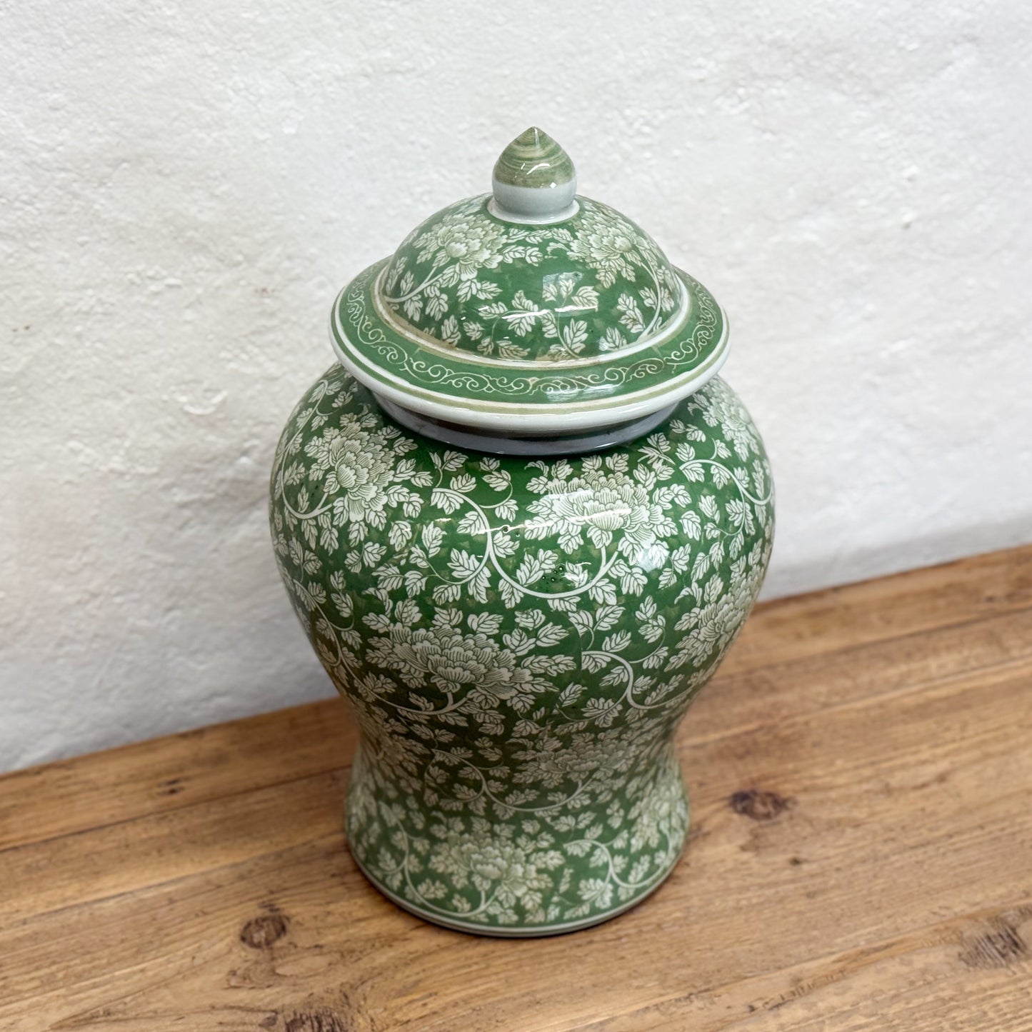 Green ceramic jar with white floral patterns on a wooden surface