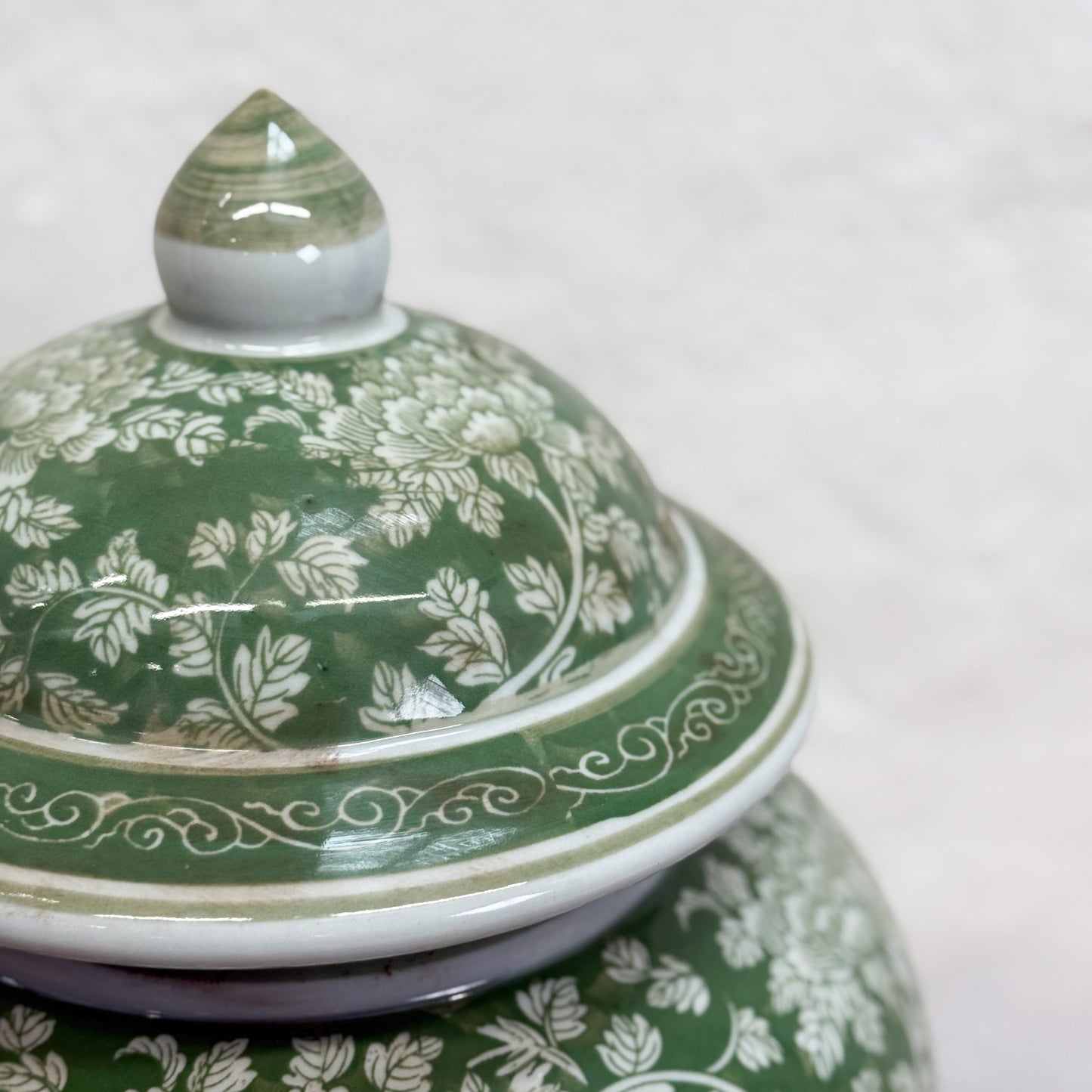 Green ceramic jar with floral patterns on a white background