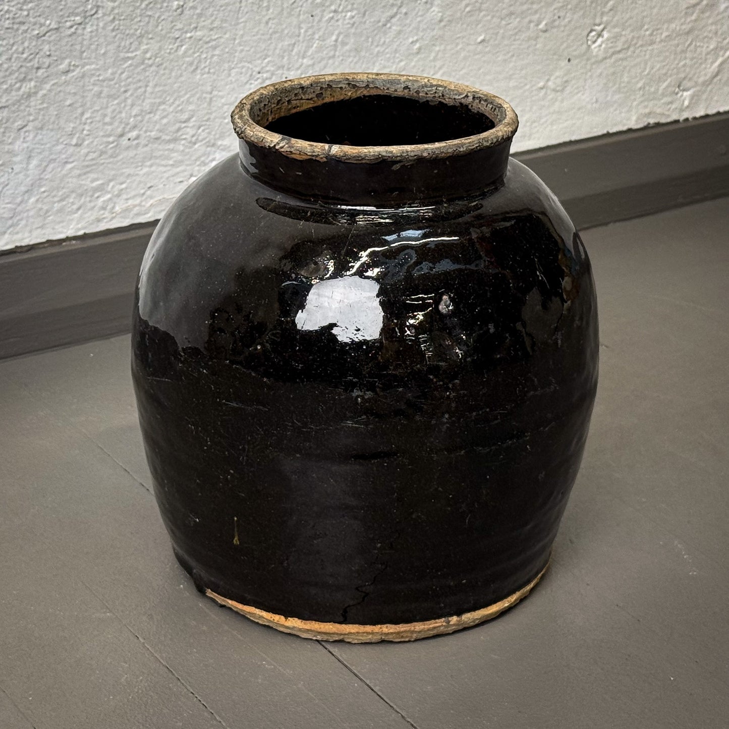 Black ceramic jar on a gray floor against a white wall