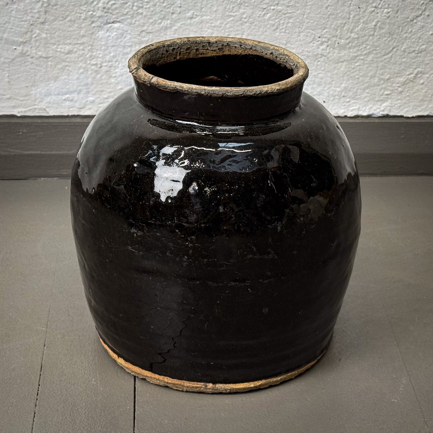 Black ceramic jar on a gray floor with a white wall background