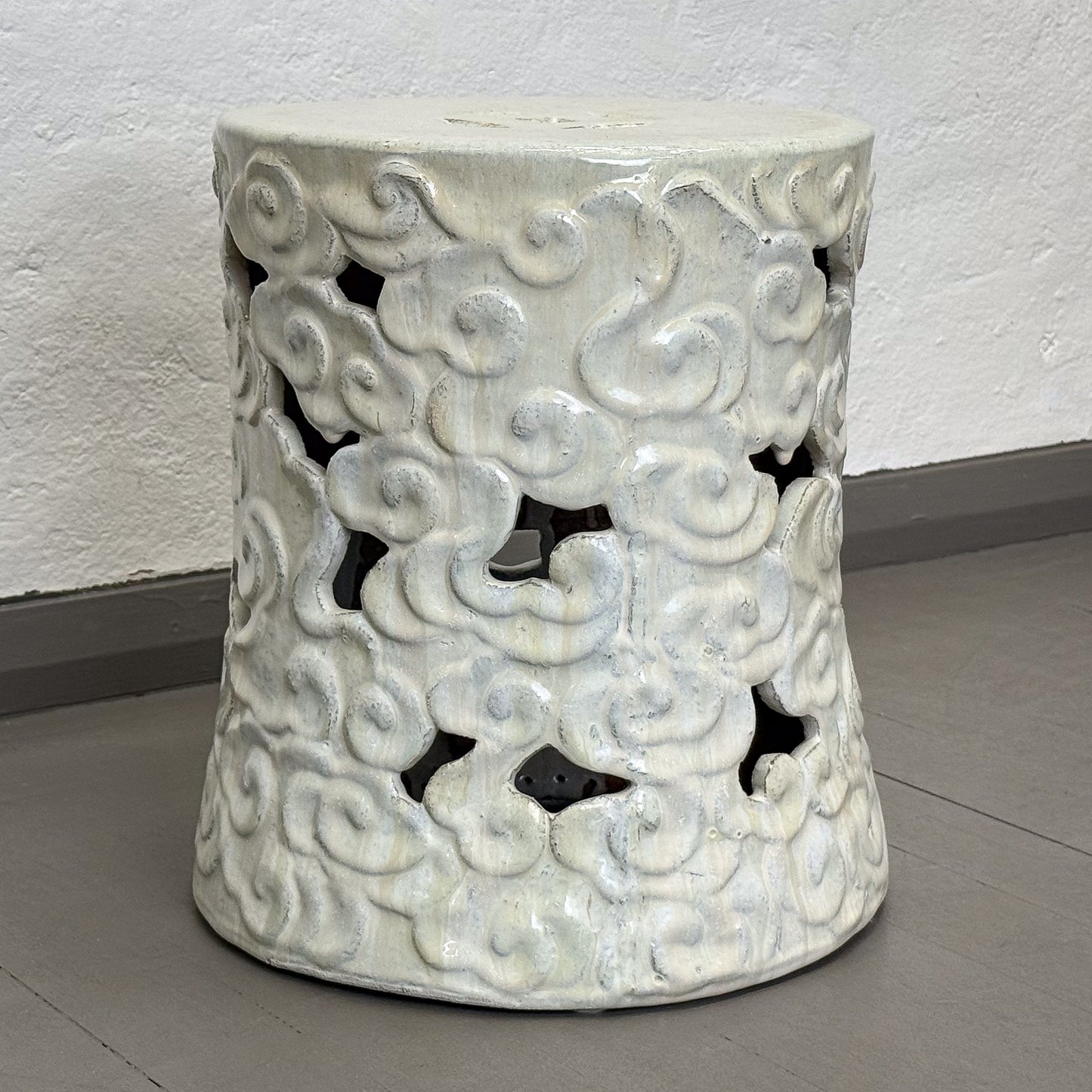 Decorative white ceramic stool with cloud patterns on a plain background