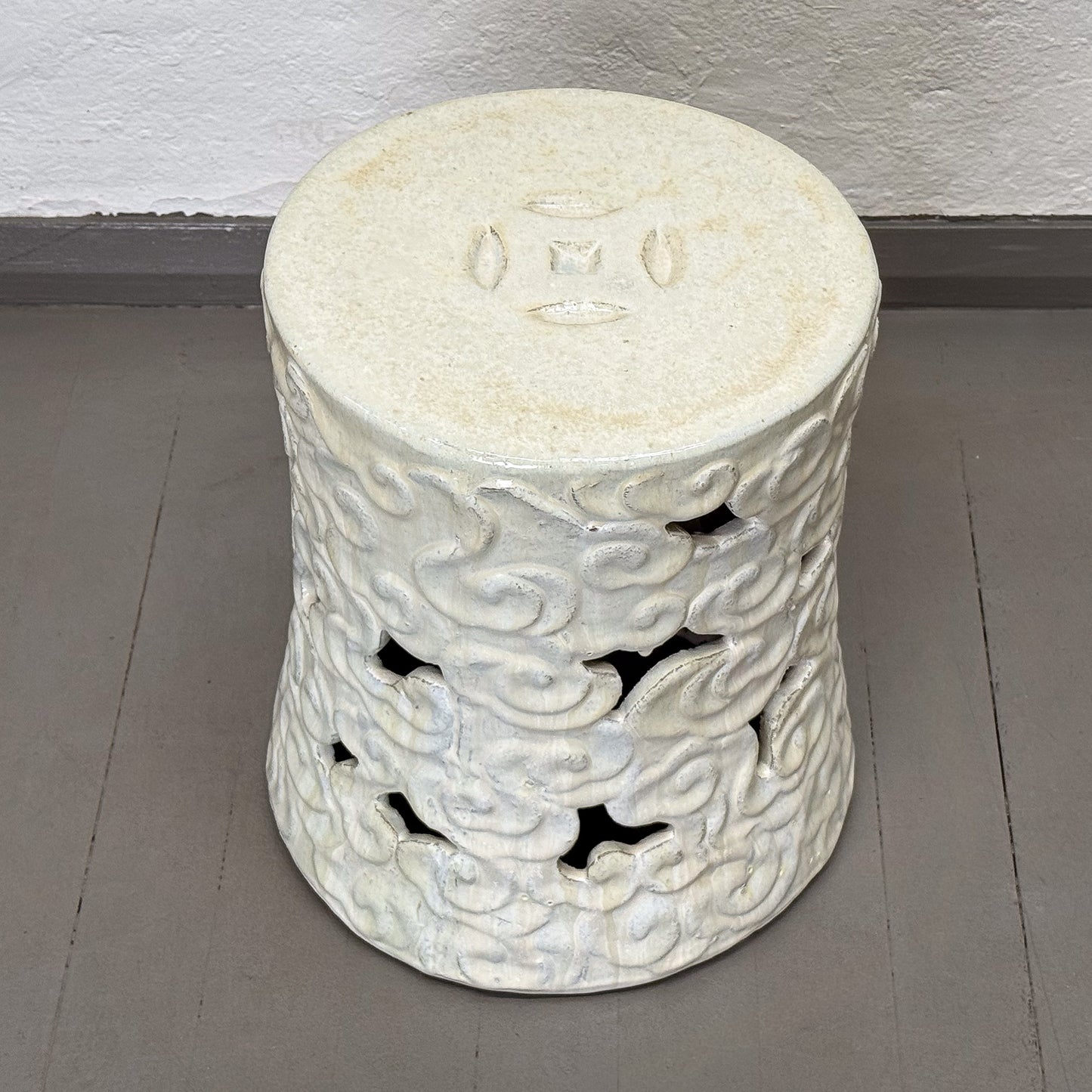Decorative white stone stool with intricate carvings on a gray floor.