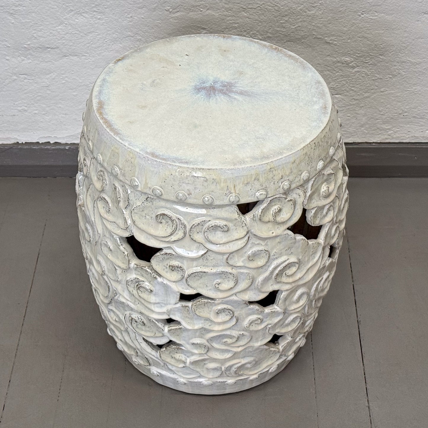 Decorative white ceramic stool with cloud patterns on a gray floor.