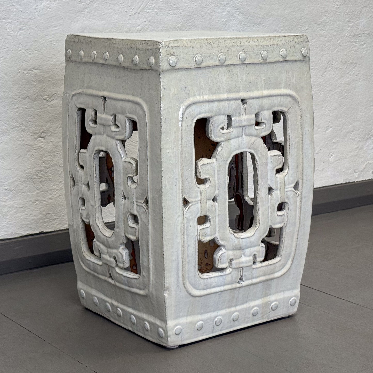 Decorative concrete stool with geometric pattern on a gray floor.