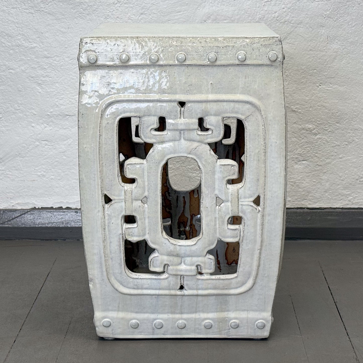 Decorative concrete stool with geometric pattern on a gray floor.