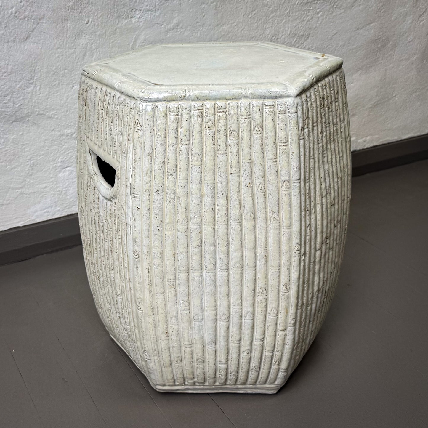 Textured white ceramic stool on a gray floor against a white wall