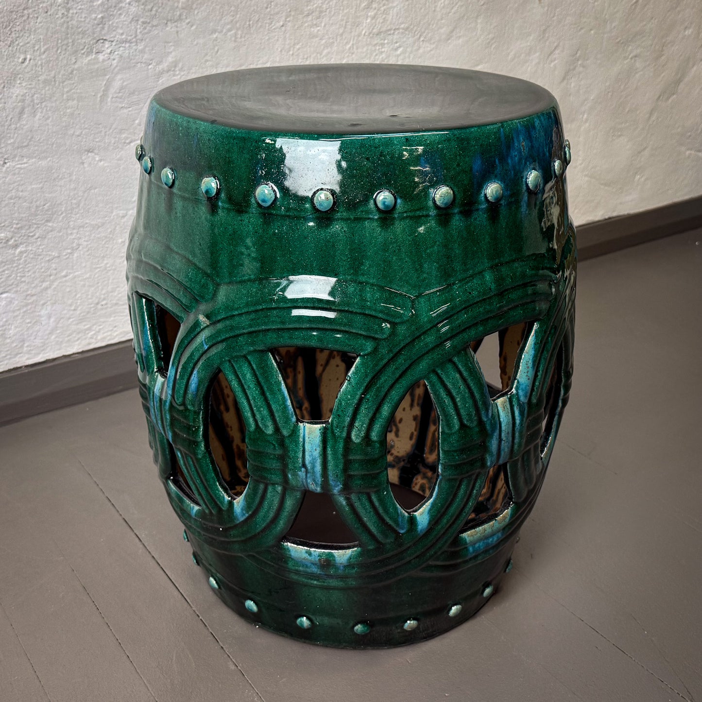 Decorative green ceramic stool with intricate patterns on a plain floor.