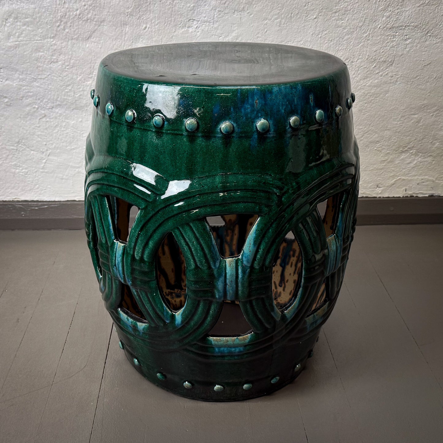 Decorative green ceramic stool with intricate patterns on a plain floor.