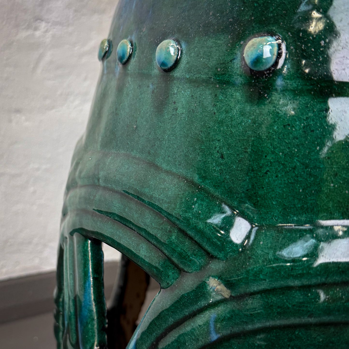 Close-up of a green ceramic vase with textured surface and reflective eyes.