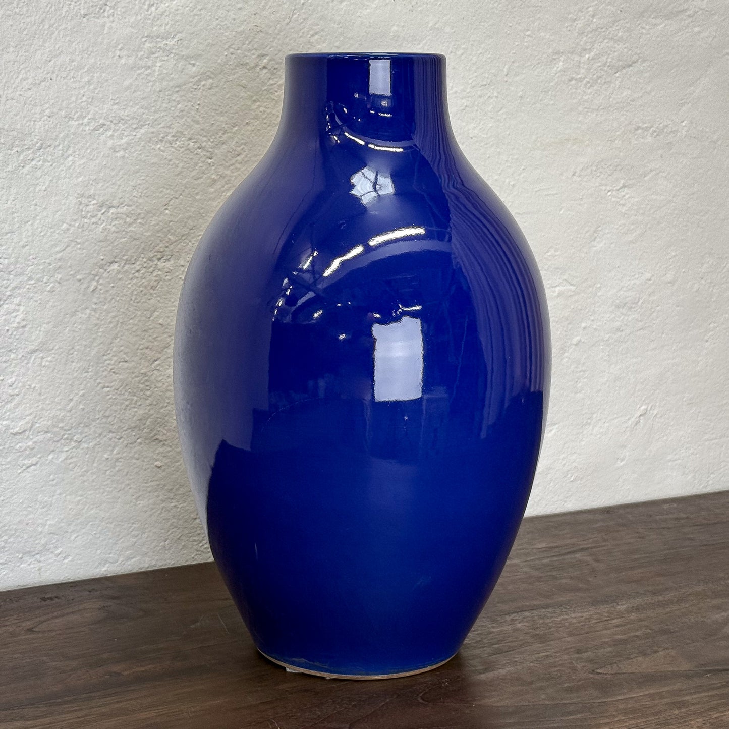 Glossy blue vase on a wooden surface with a textured white wall background