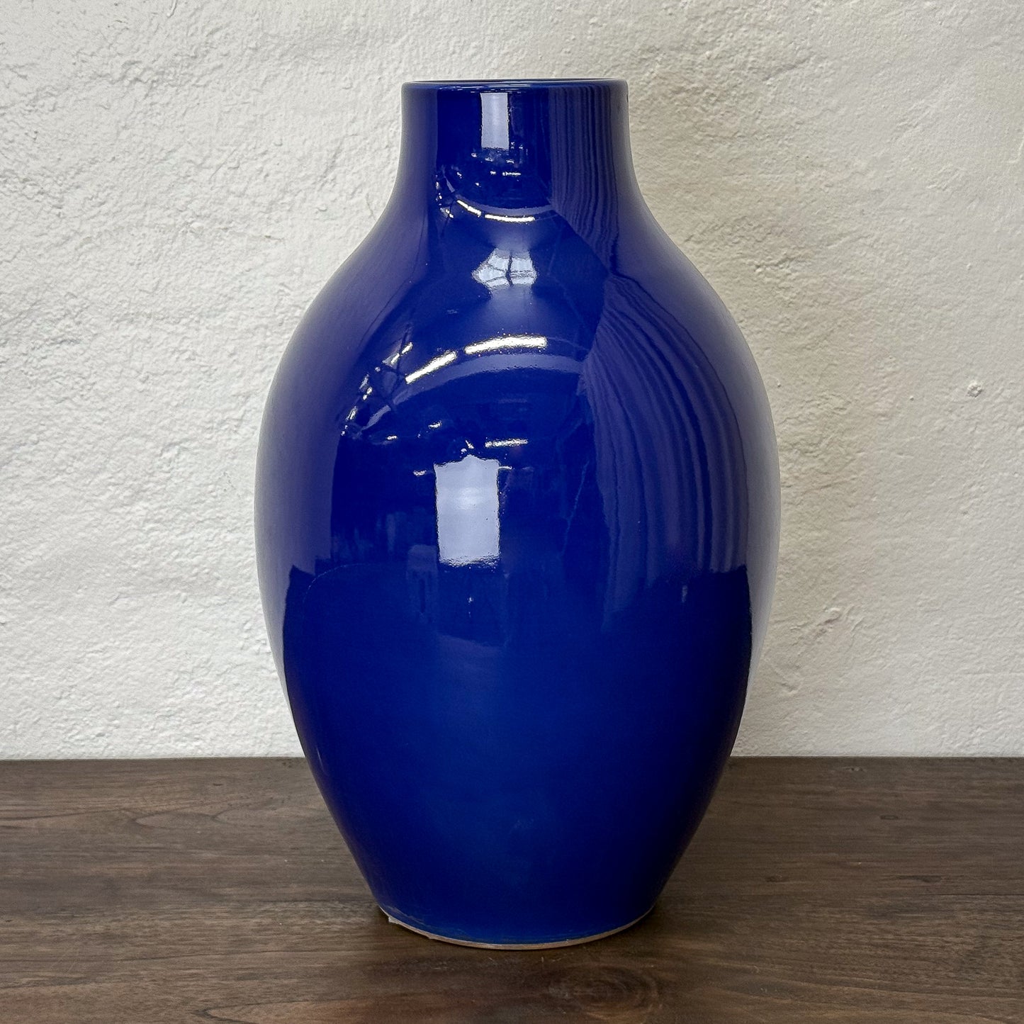 Glossy blue vase on a wooden surface with a textured white wall background