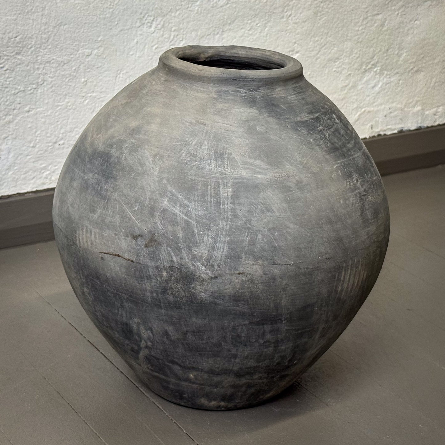 Large gray clay pot on a plain floor with a white wall background