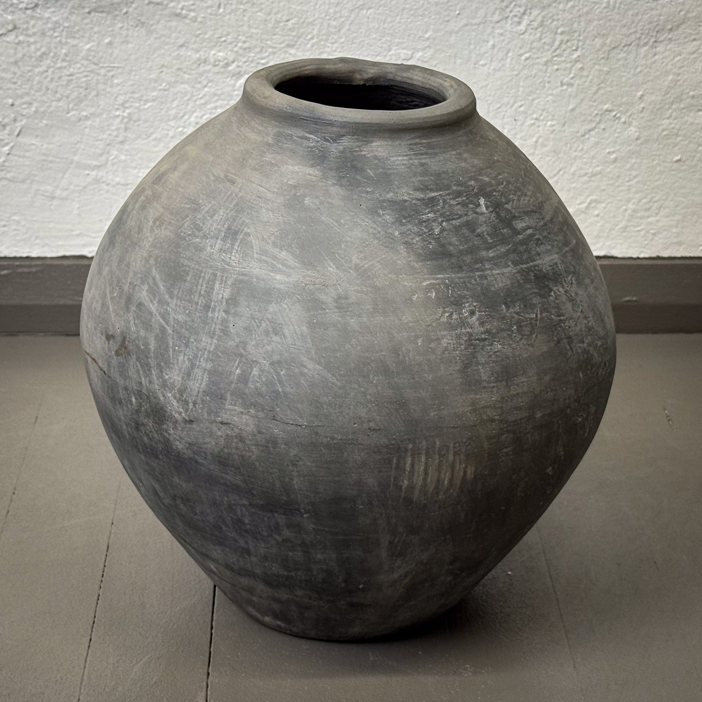 Large gray clay pot on a plain floor with a white wall background