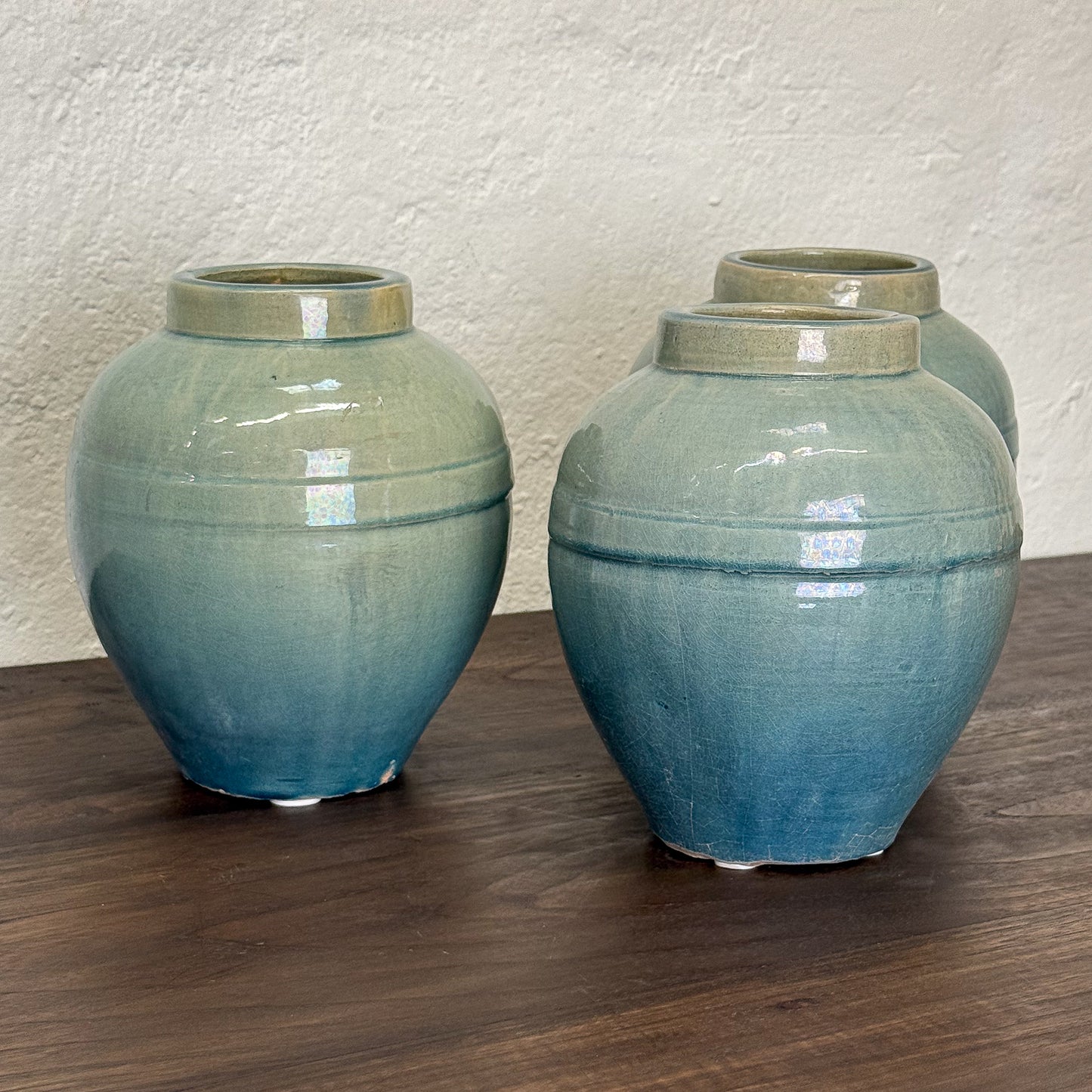 Three blue ceramic jars on a wooden surface with a beige wall background