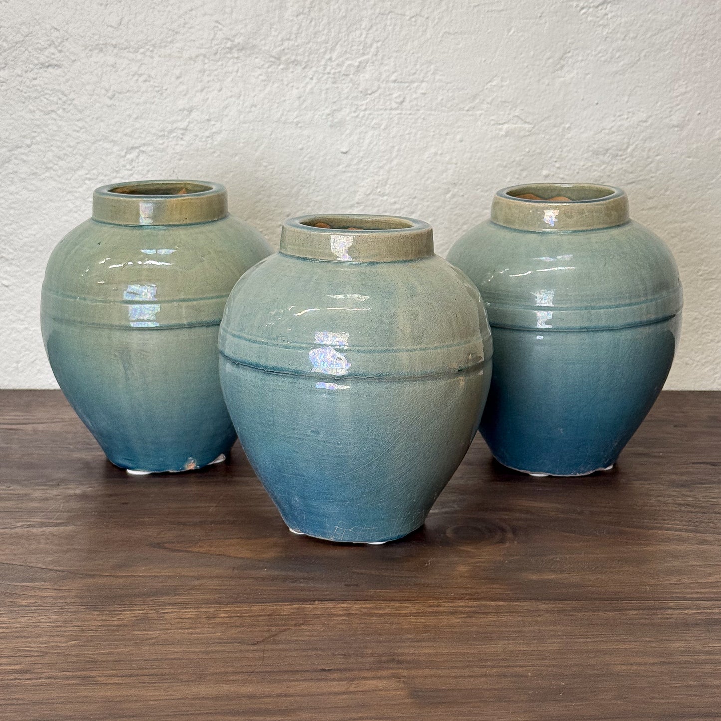 Three blue ceramic jars on a wooden surface with a beige wall background