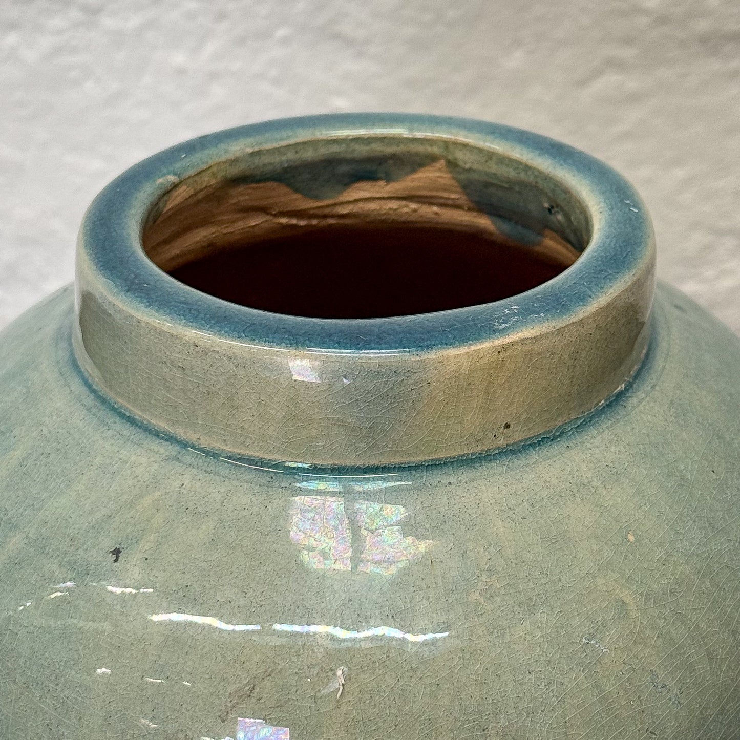 Close-up of a ceramic vase with a ribbed texture and blue rim on a textured gray background