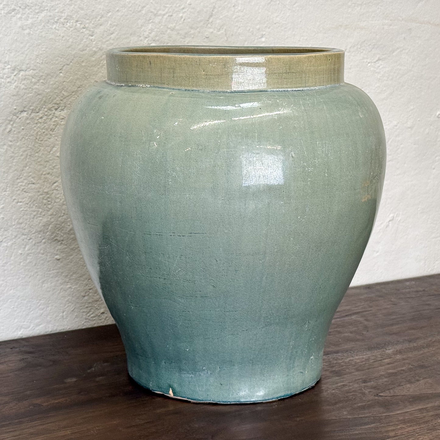 Green ceramic jar on a wooden surface with a white textured wall background