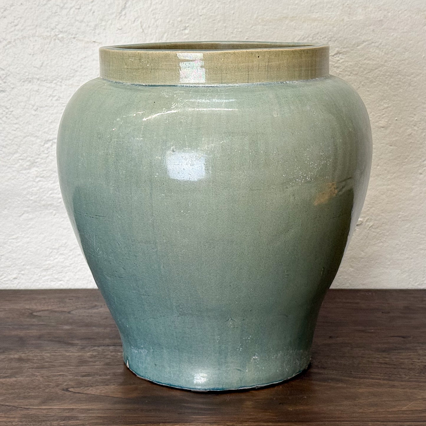 Green ceramic jar on a wooden surface with a white textured wall background