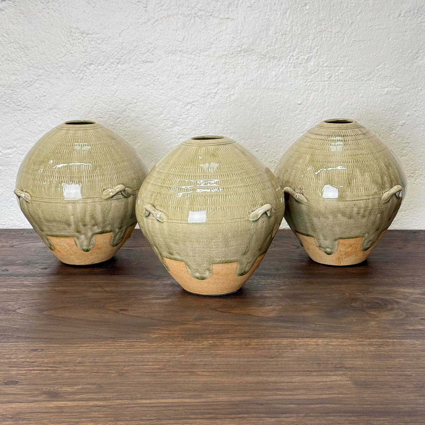 Three green ceramic vases with ribbed texture on a wooden surface.