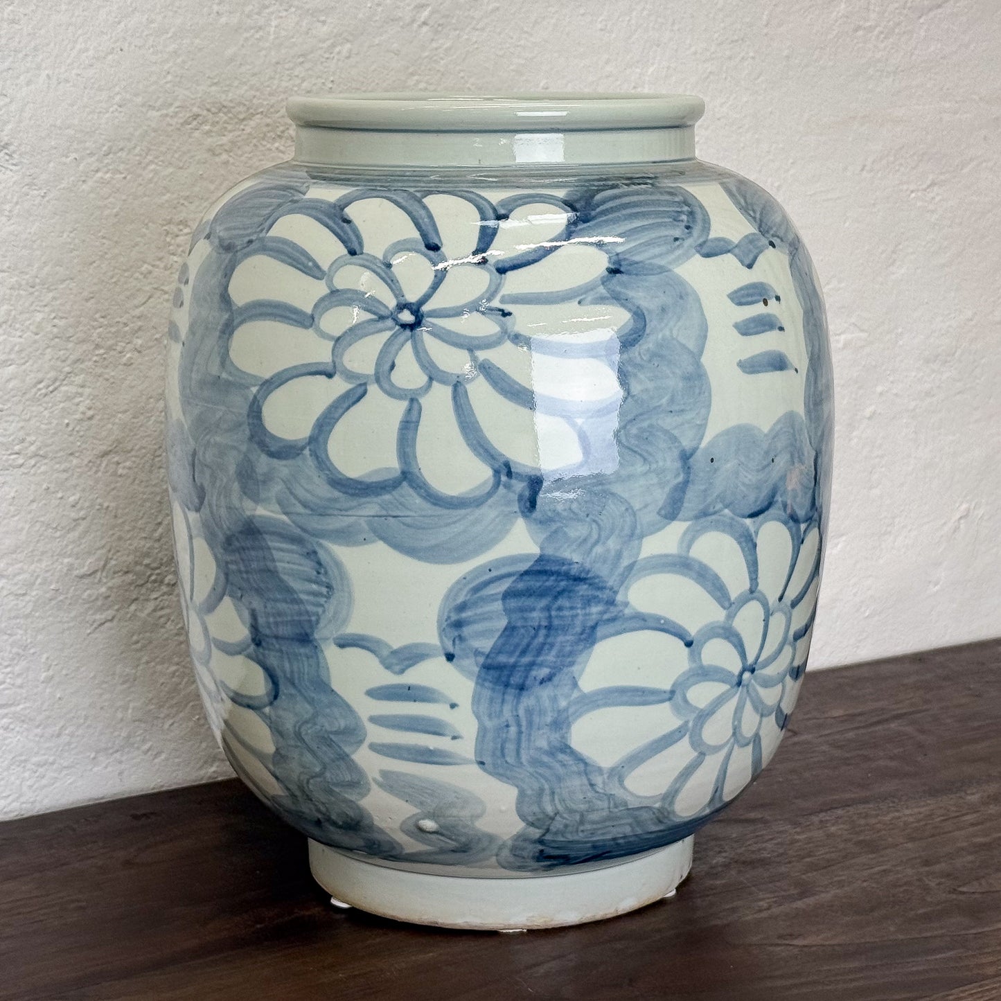 Ceramic vase with blue floral patterns on a wooden surface and white wall background