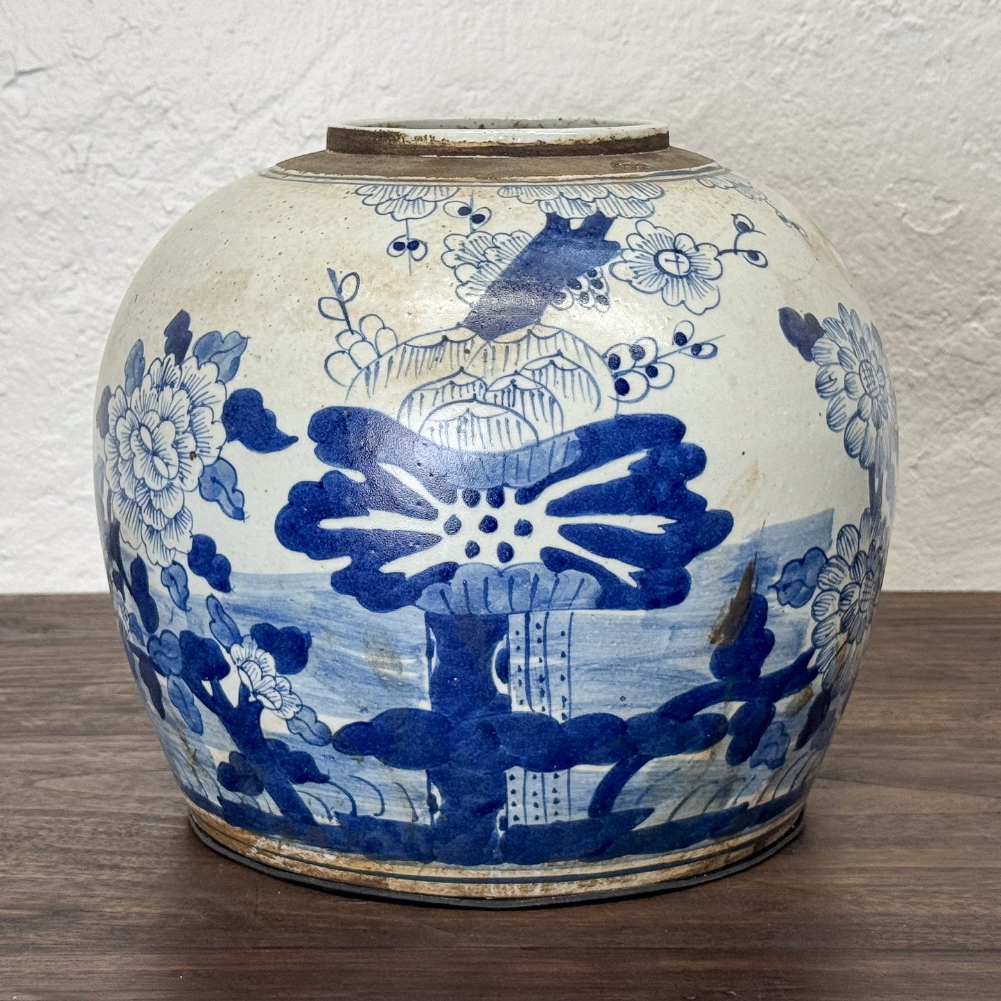 Blue and white ceramic jar with floral and architectural designs on a wooden surface.