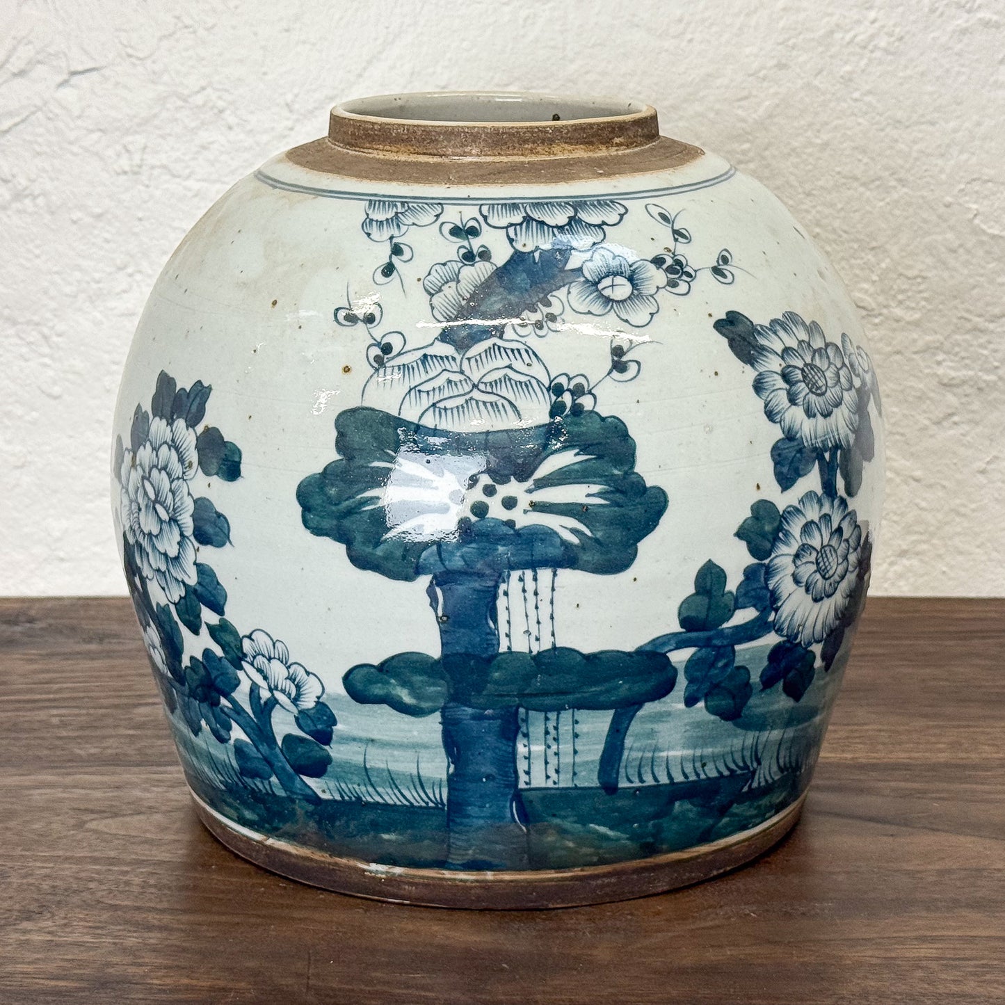 Blue and white ceramic jar with floral and landscape design on a wooden surface.
