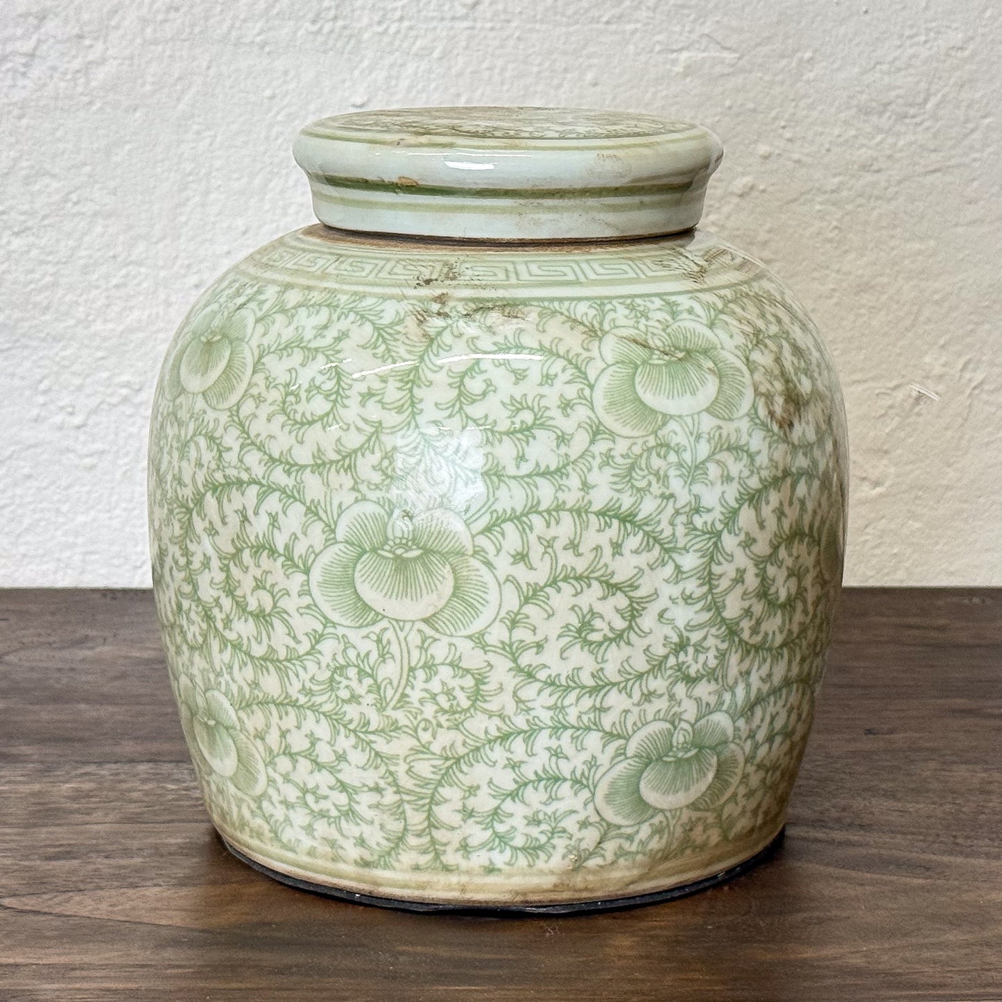Green ceramic jar with floral patterns on a wooden surface