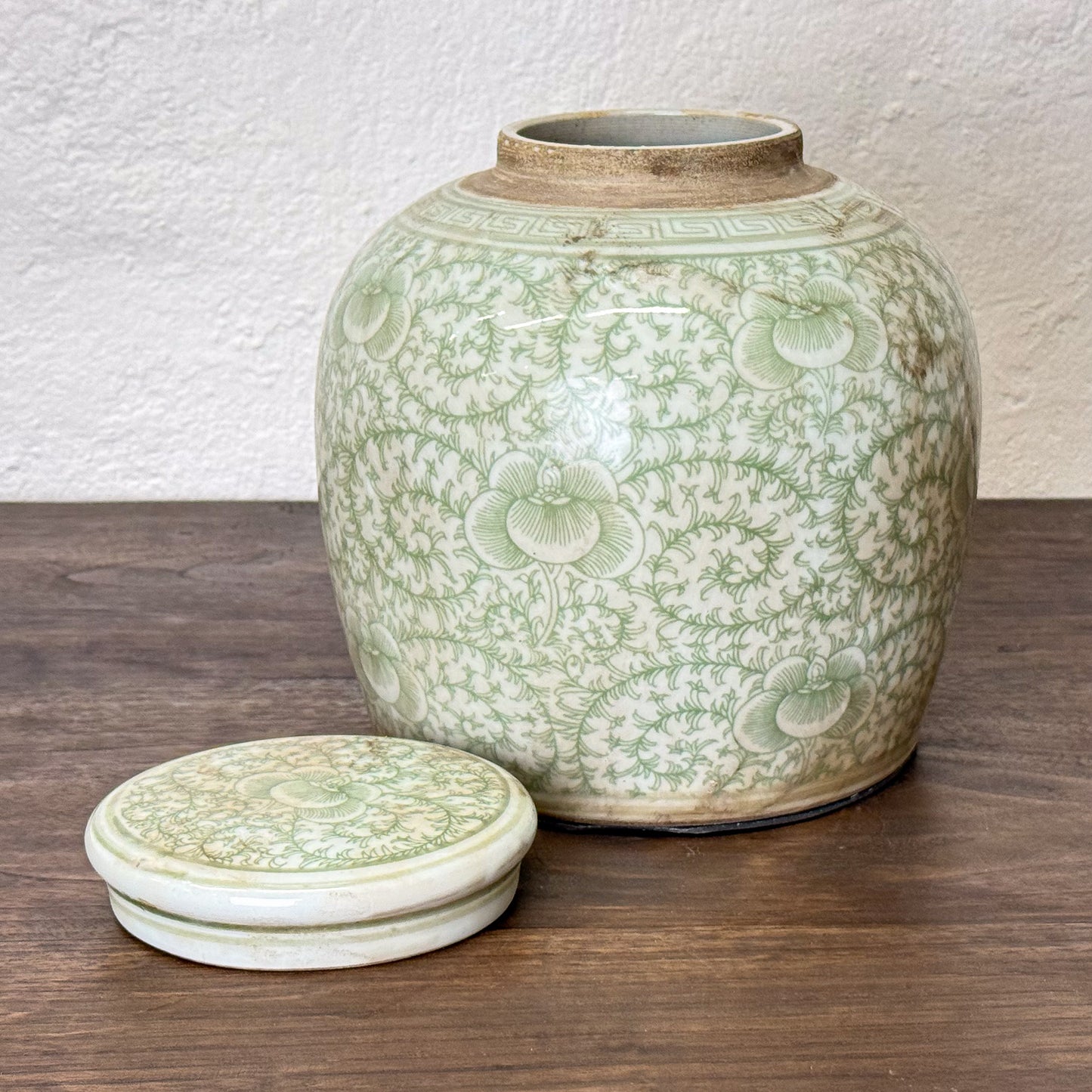 Green ceramic jar with floral patterns on a wooden surface