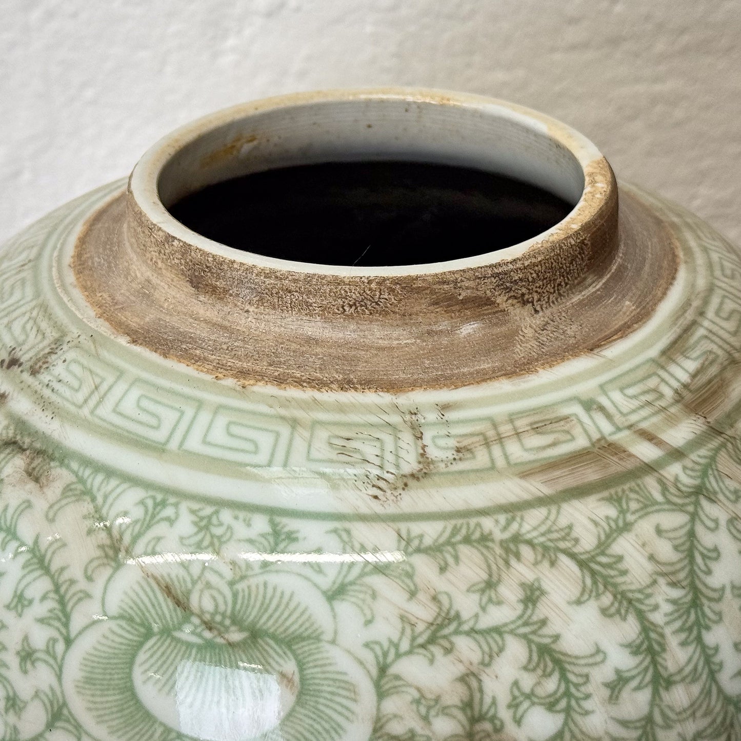 Close-up of a ceramic jar with green floral patterns on a white background