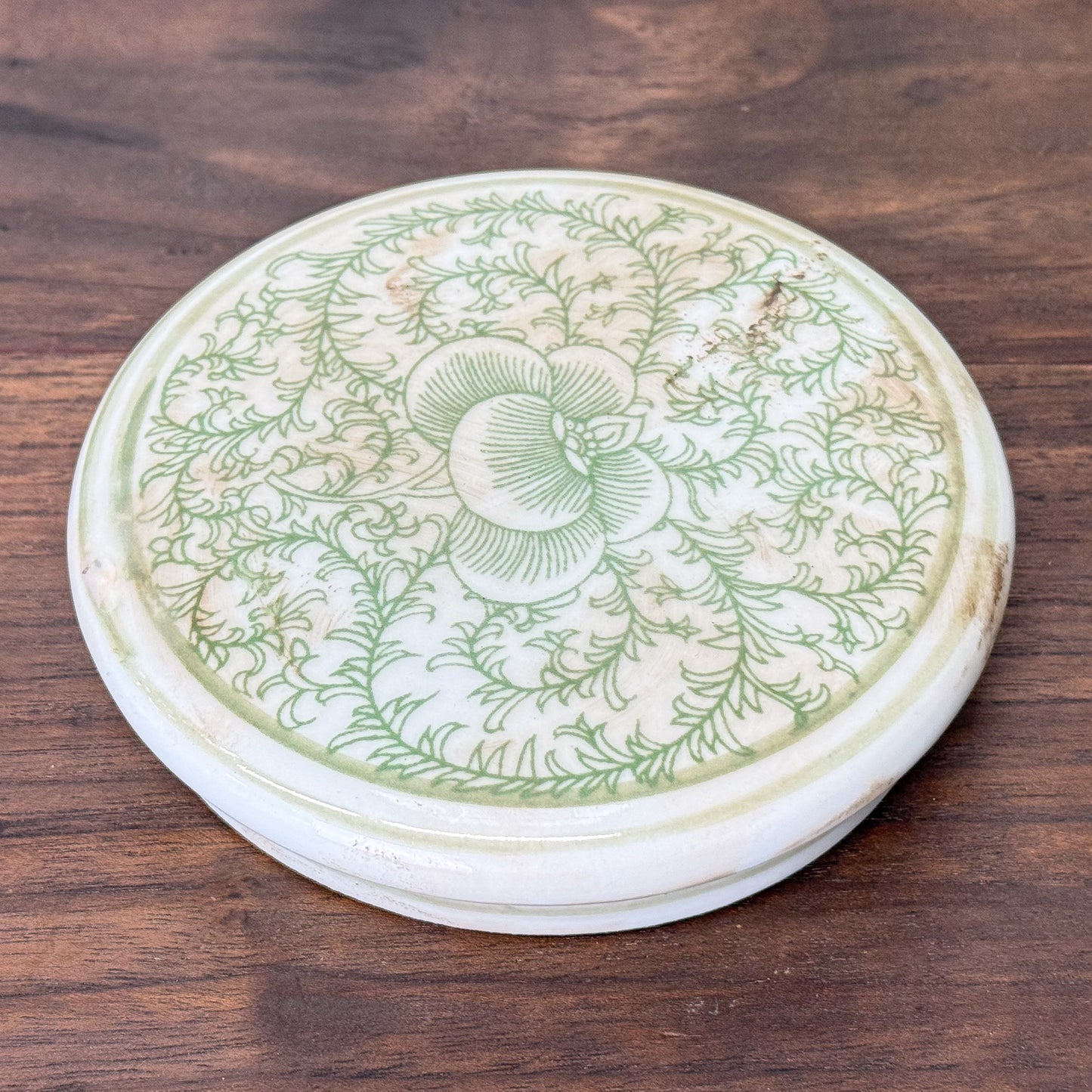 Decorative ceramic lid with green floral patterns on a wooden surface