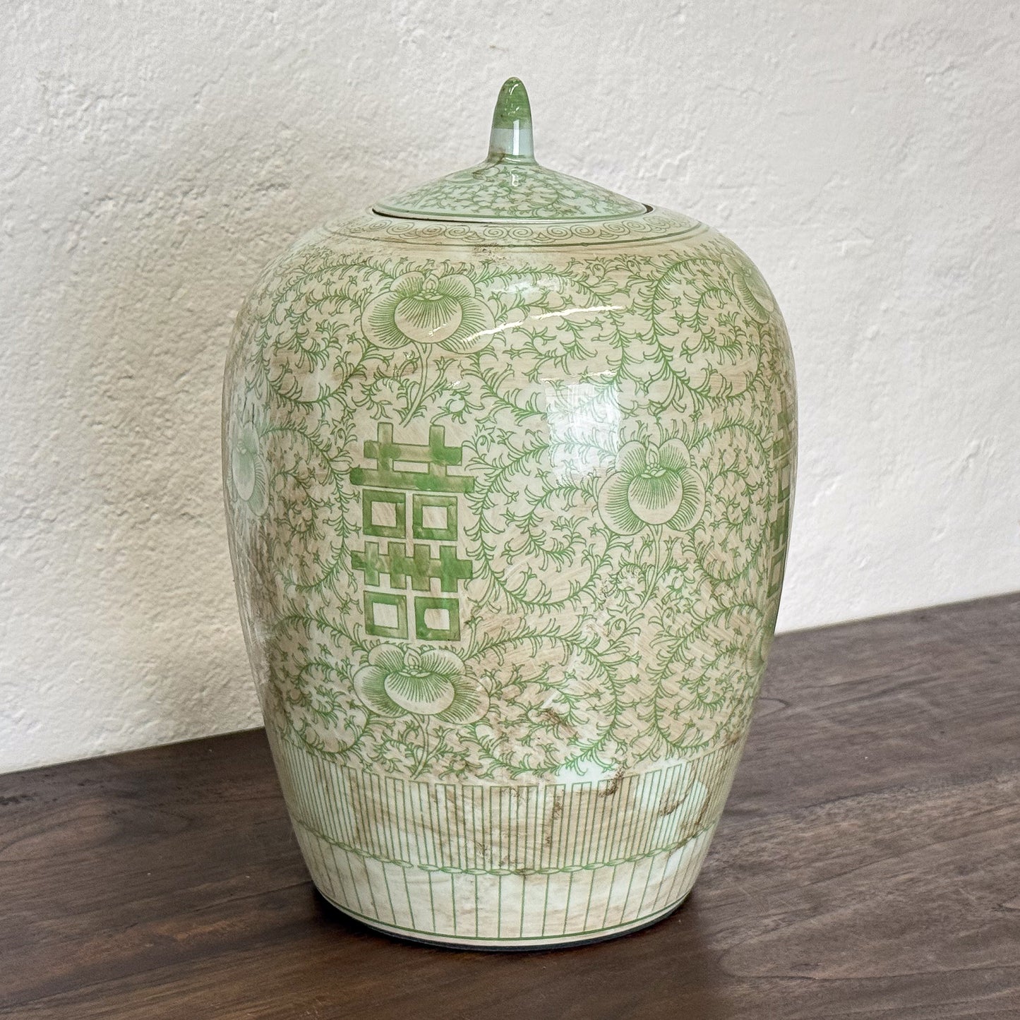 Green ceramic jar with intricate patterns on a wooden surface