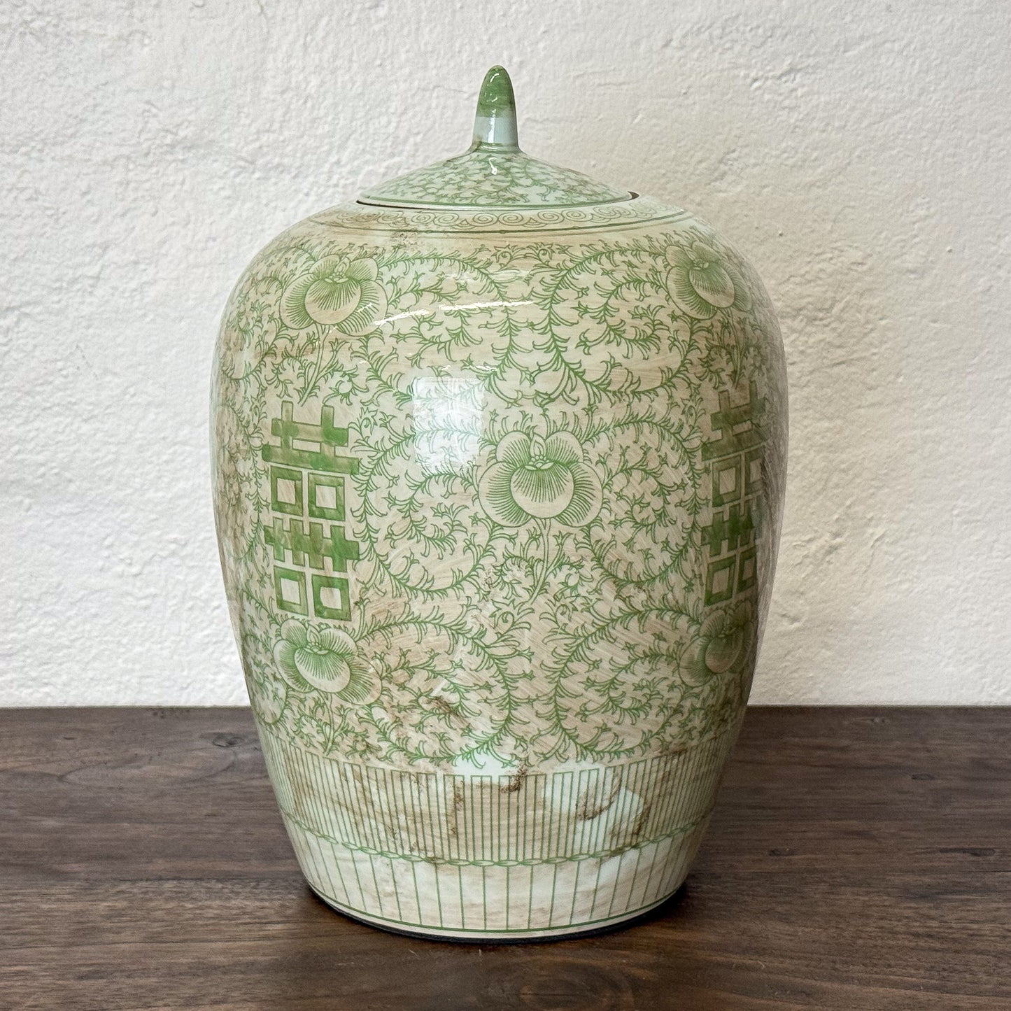 Green ceramic jar with intricate patterns on a wooden surface