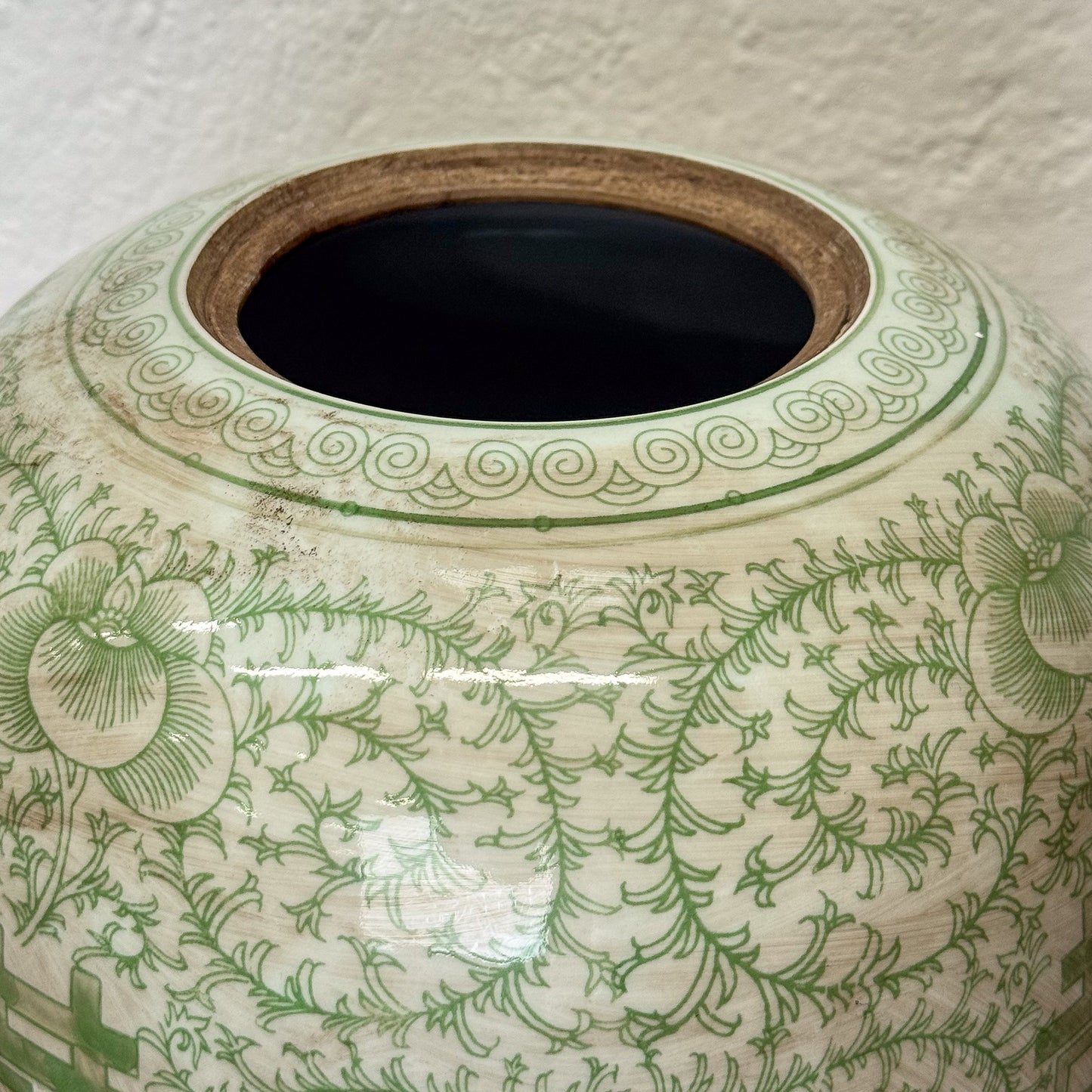 Close-up of a ceramic jar with green floral patterns on a textured surface