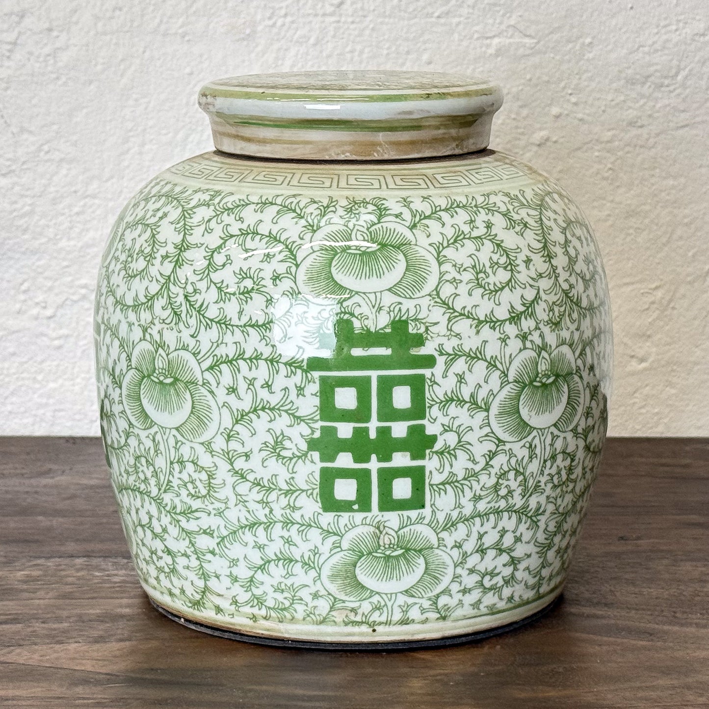 Green and white ceramic jar with floral patterns and a double happiness symbol on a wooden surface.