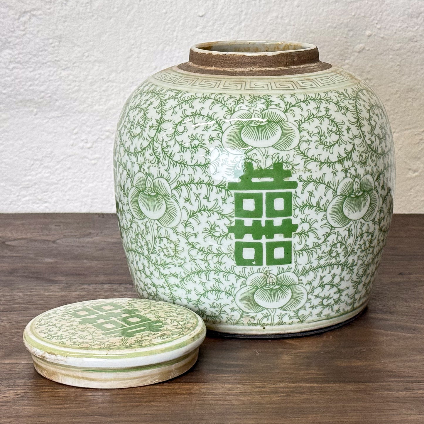 Green ceramic jar with floral patterns and a lid on a wooden surface