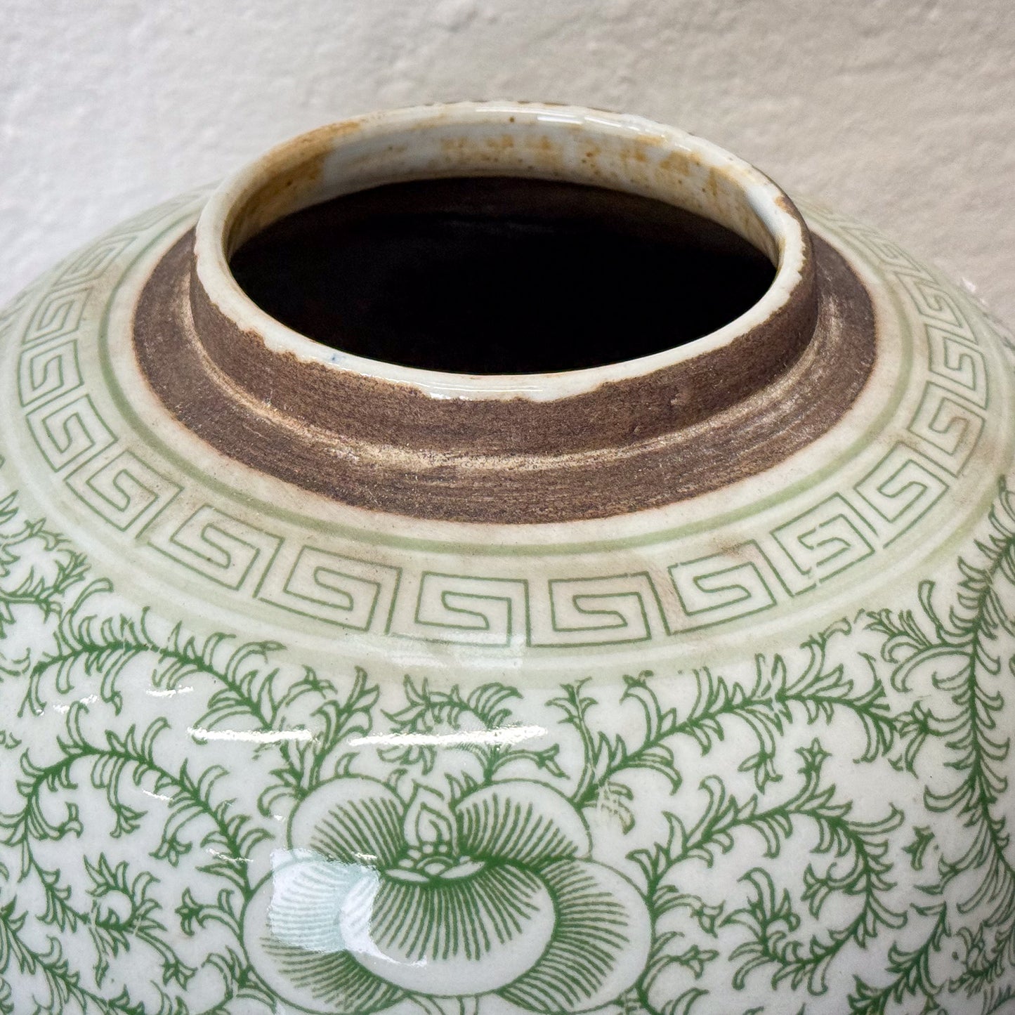 Green and white ceramic jar with floral patterns and a double happiness symbol on a wooden surface.
