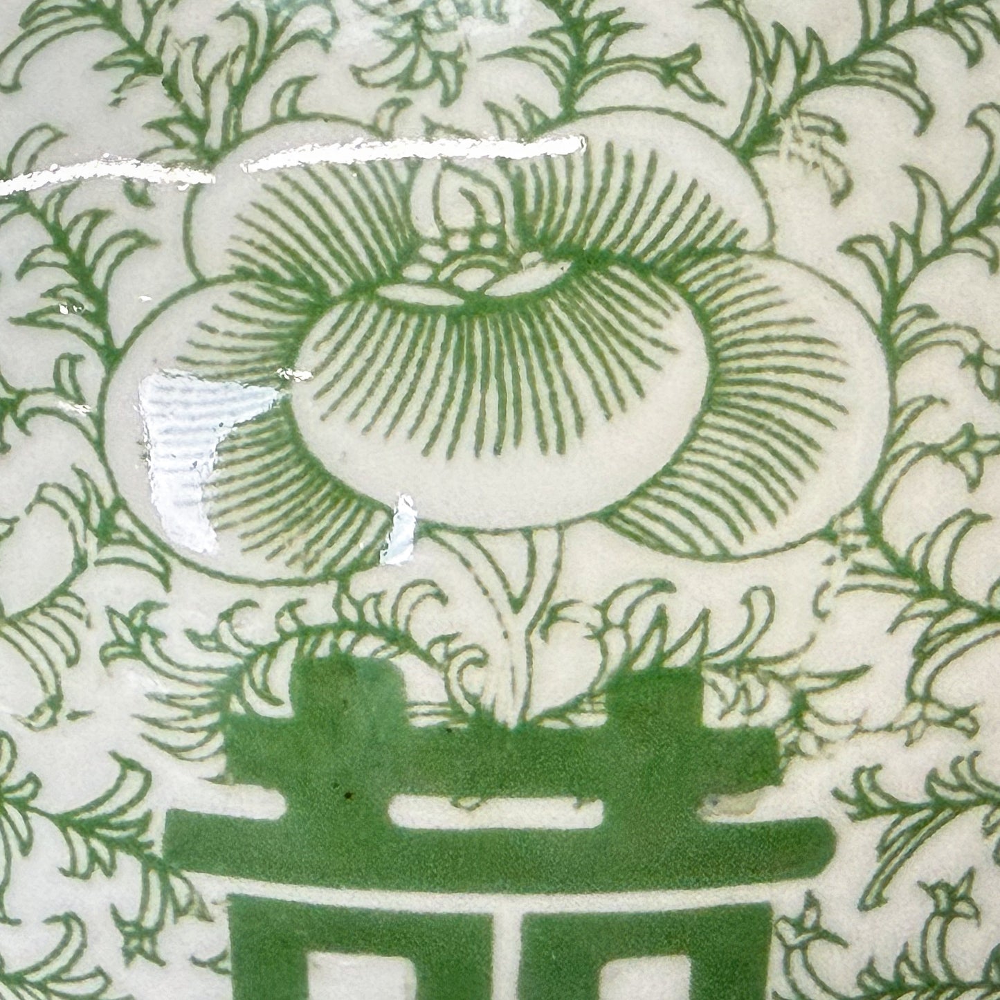 Green and white ceramic jar with floral patterns and a double happiness symbol on a wooden surface.