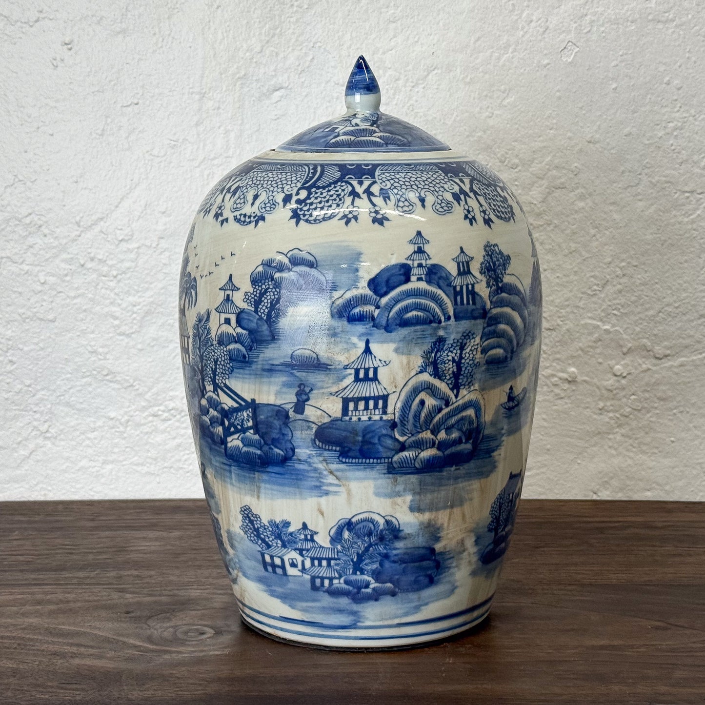 Blue and white ceramic jar with landscape design on a wooden surface and white wall background