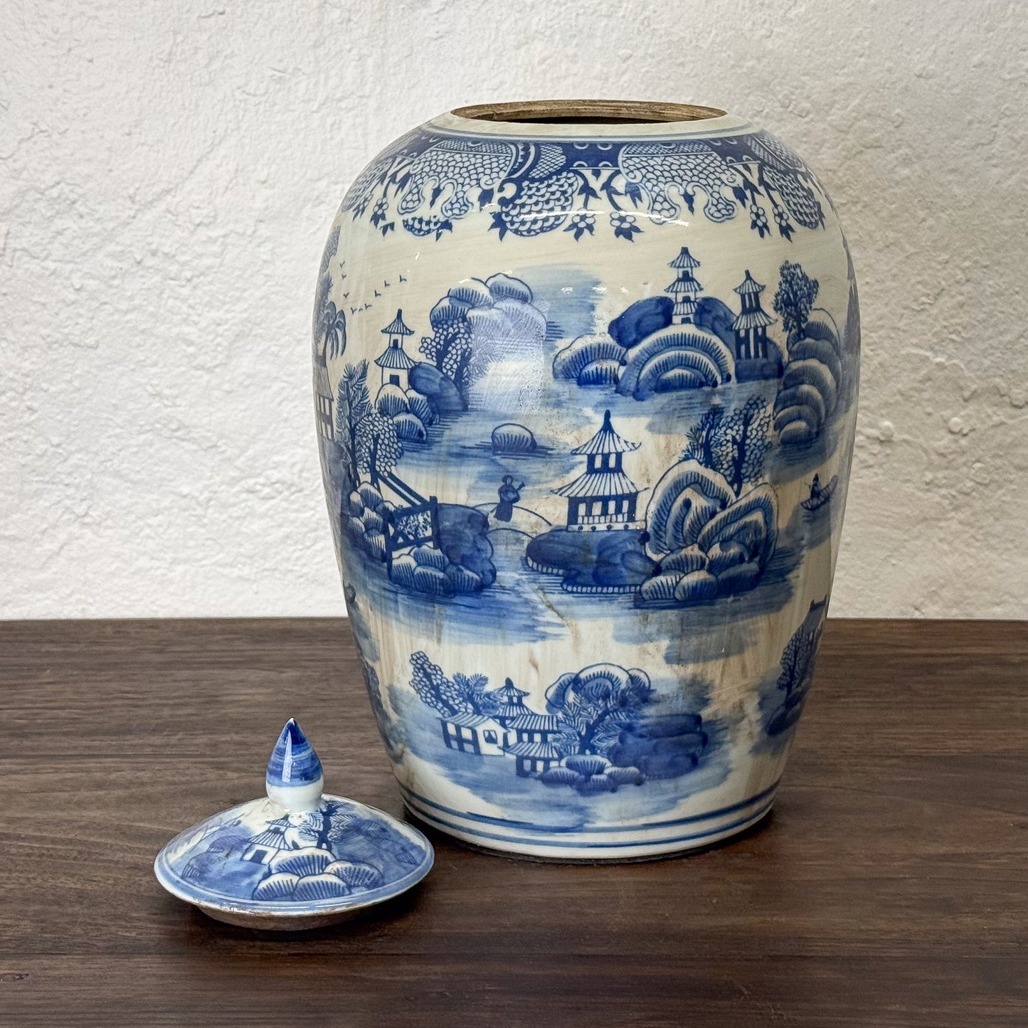 Blue and white ceramic jar with lid on a wooden surface against a textured wall.