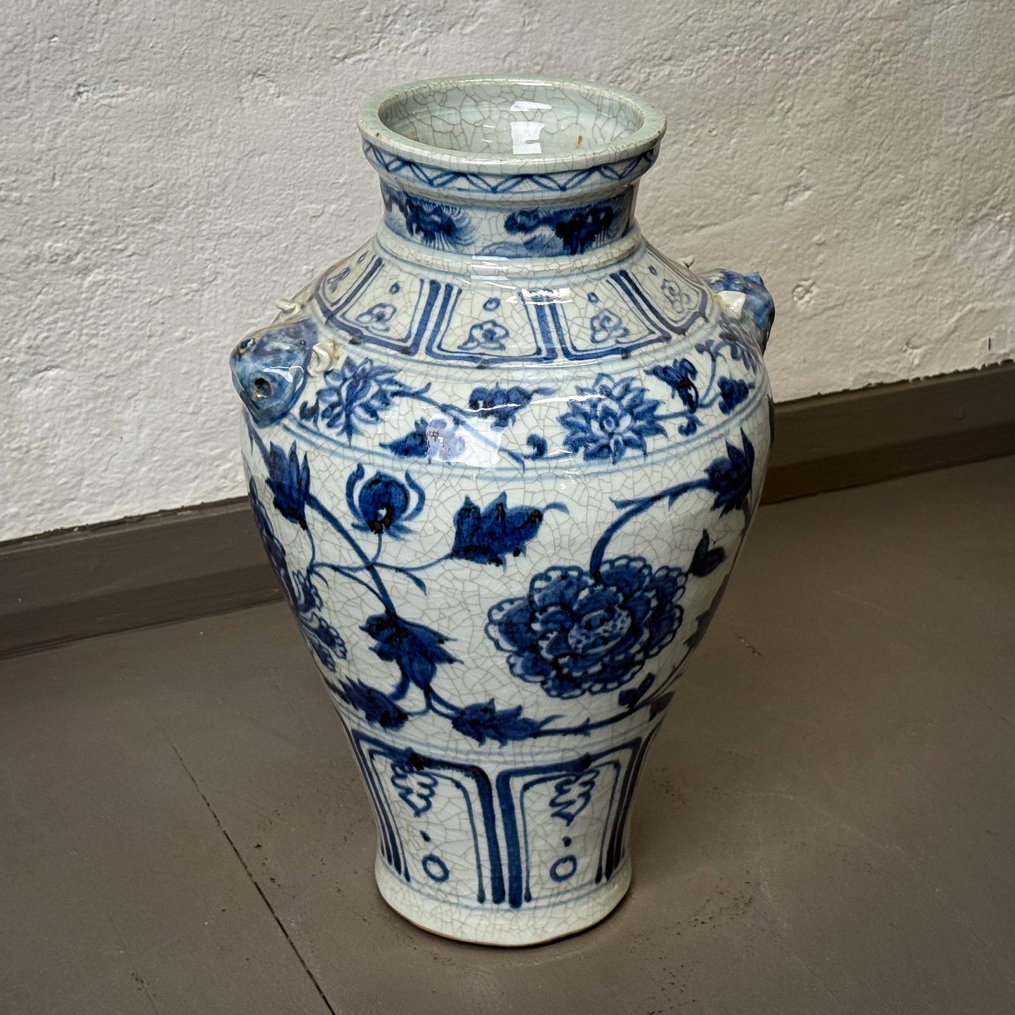 Blue and white ceramic vase with floral patterns on a plain floor.