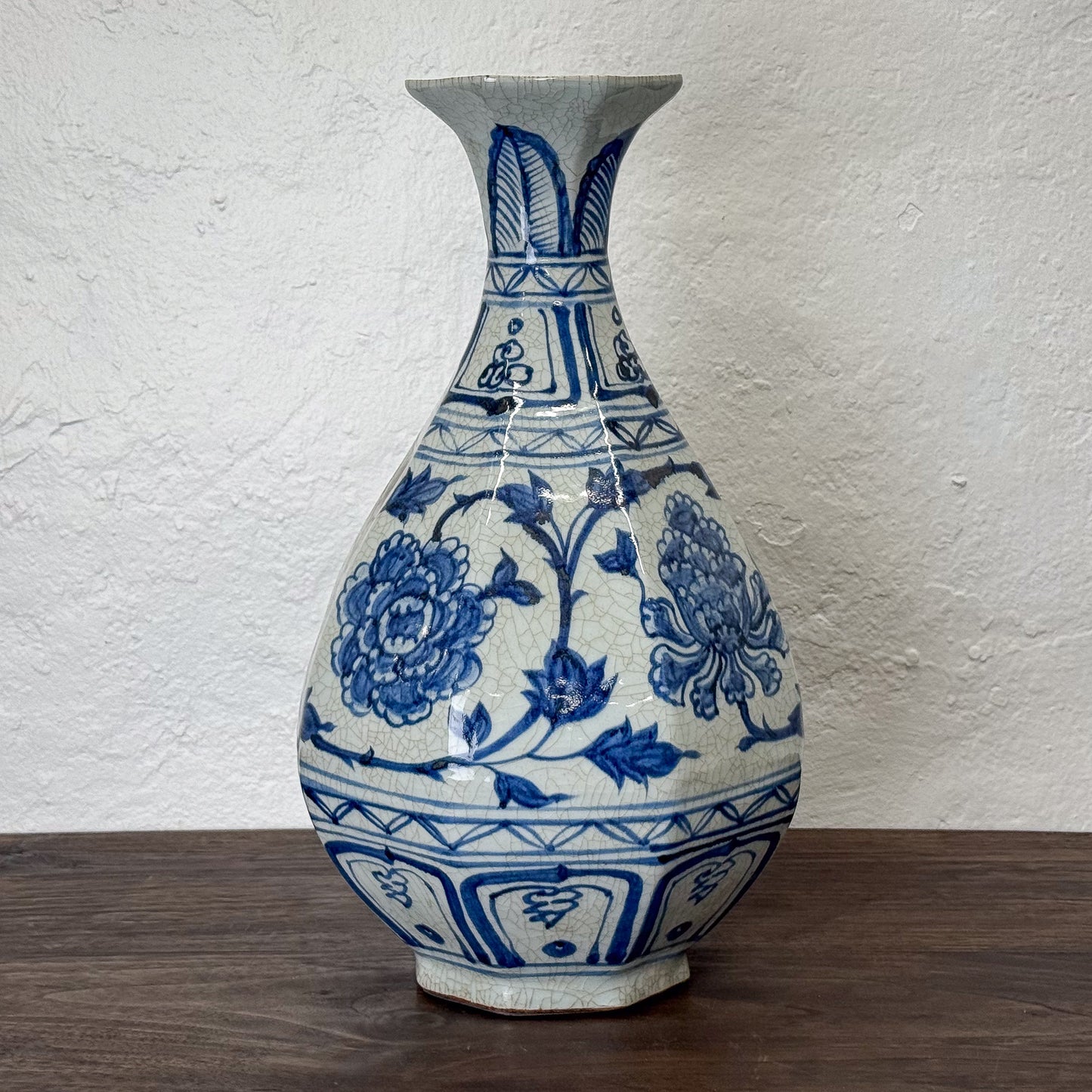Blue and white ceramic vase with floral patterns on a wooden surface and white textured wall background