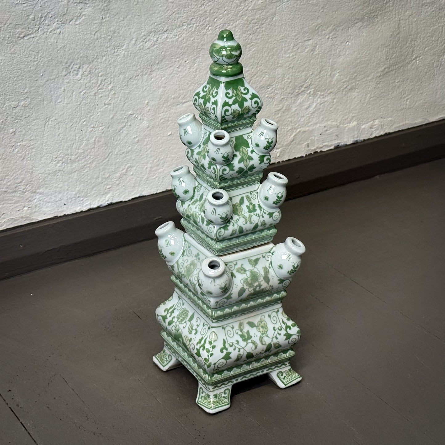 Green ceramic pagoda-like structure on a gray floor against a white wall.
