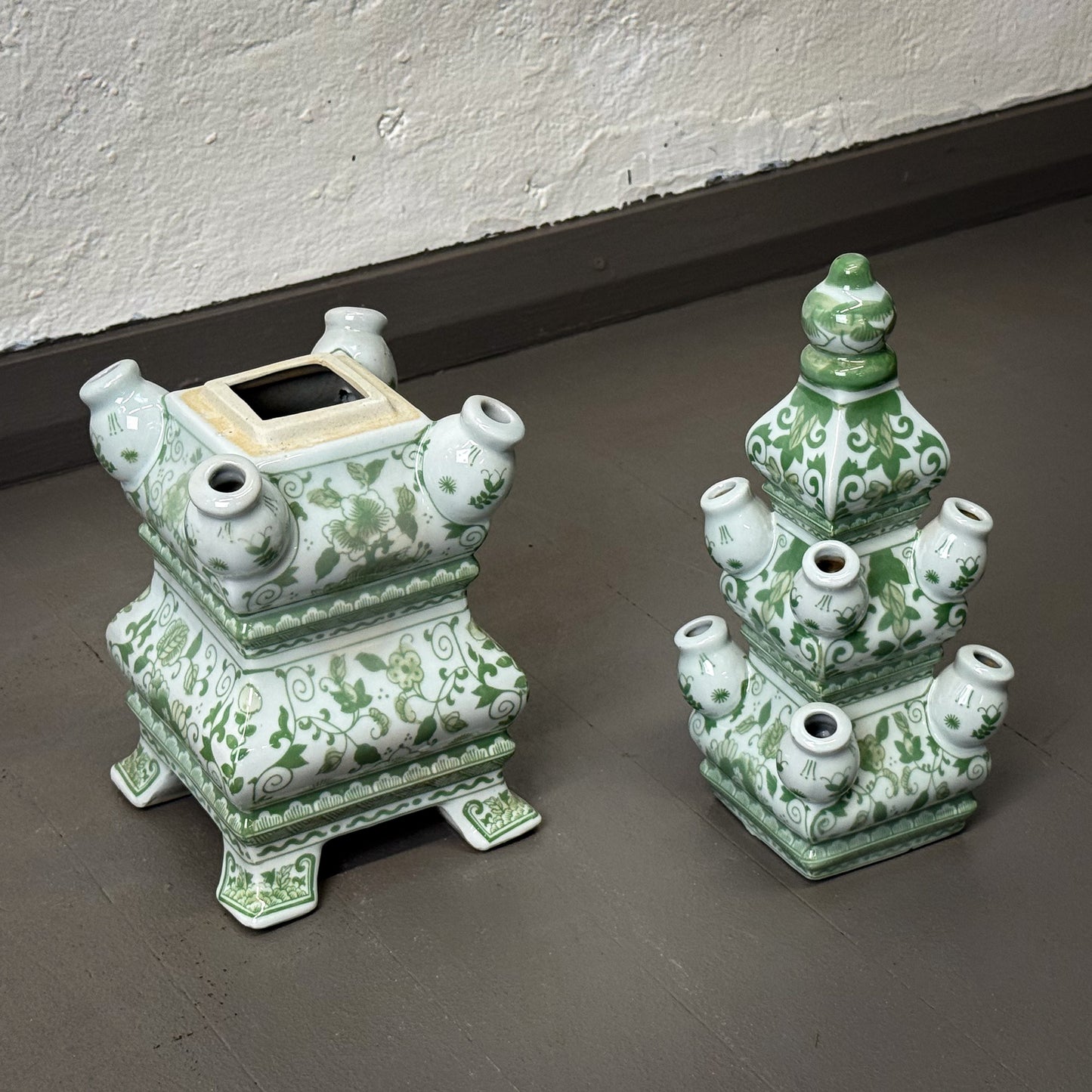 Two green and white ceramic vases on a gray floor.
