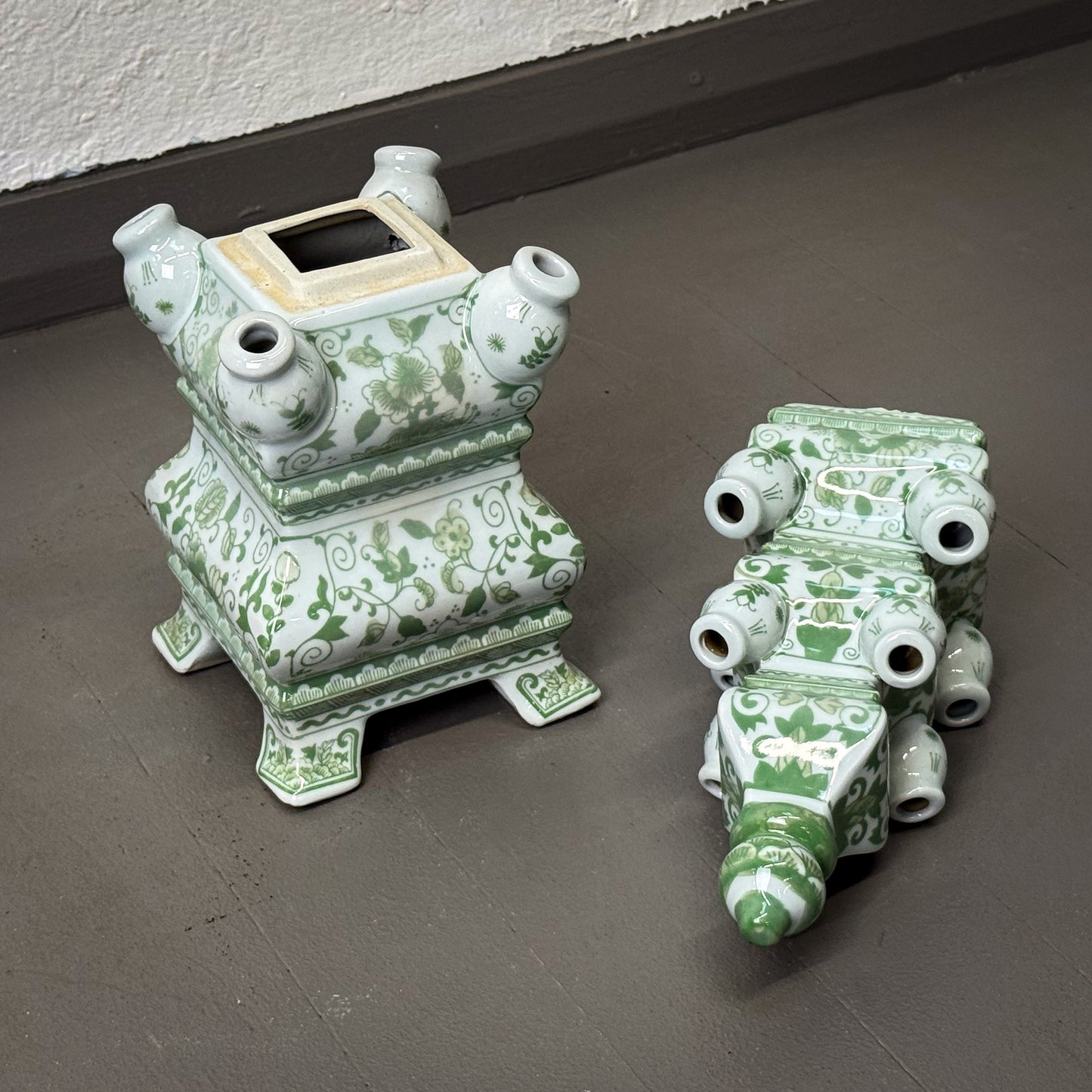 Two green and white ceramic pots on a gray floor.