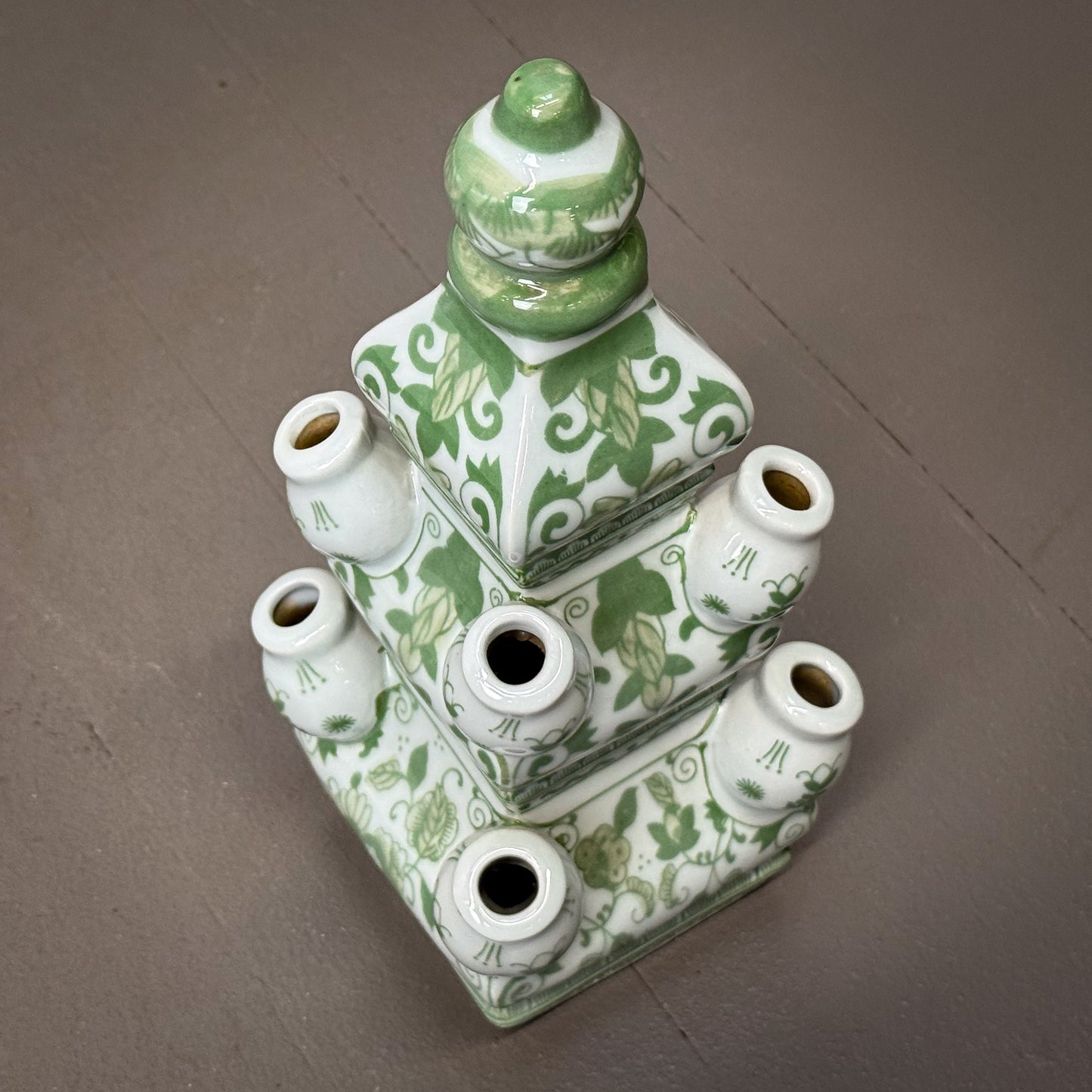 Green and white ceramic vase with multiple small necks on a gray surface