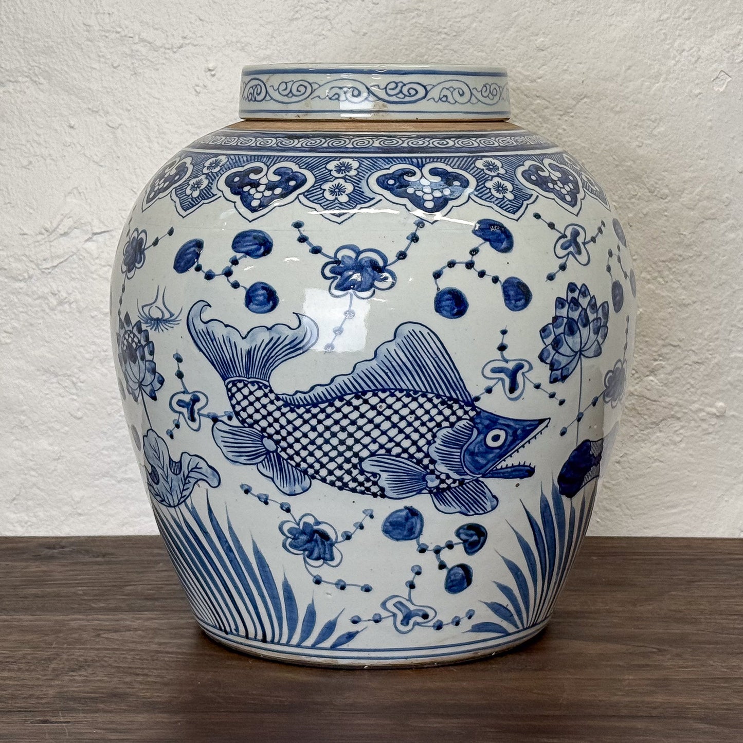 Blue and white ceramic jar with fish and floral patterns on a wooden surface.